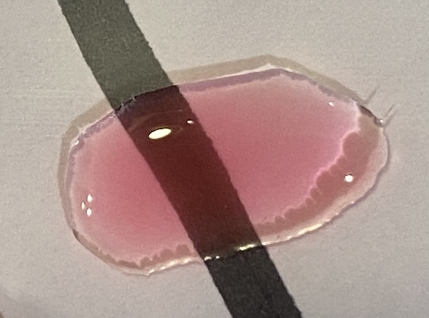 Bilde av fargeprøve tatt i lampelys, hvitt ark med sort tusjstrek som bakgrunn for å vise dekkevne.